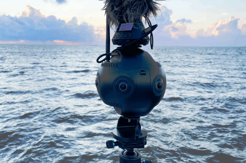 Insta 360 pro 2 camera with a microphone on top in front of the ocean with sunset.