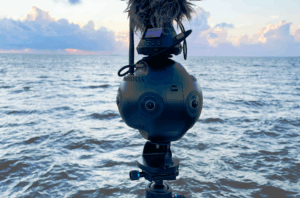 Insta 360 pro 2 camera with a microphone on top in front of the ocean with sunset.