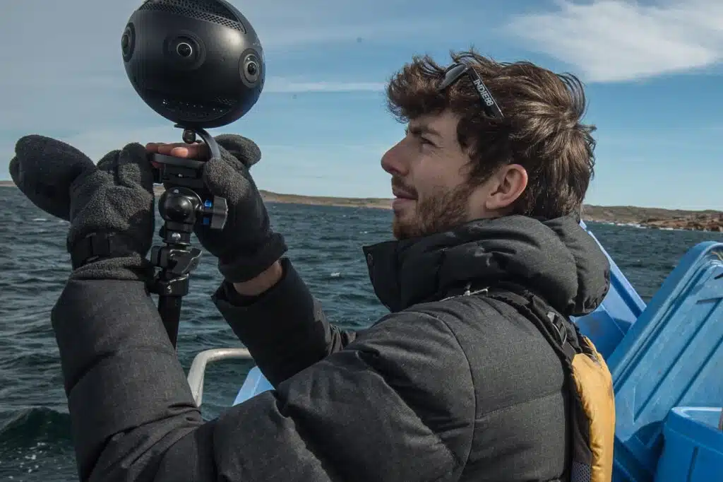 Vidéaste réglant une caméra professionnelle Insta360 Pro 2 sur un trépied à bord d'un bateau lors d'un tournage en extérieur.