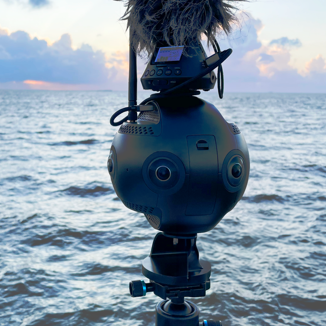 Insta 360 pro 2 camera with a microphone on top in front of the ocean with sunset.